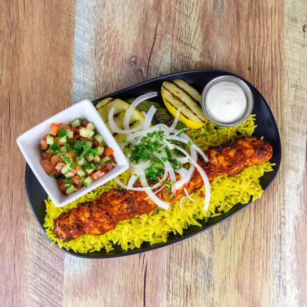 Chicken skewer with yellow rice, grilled vegetables, salsa, and a side of white sauce.