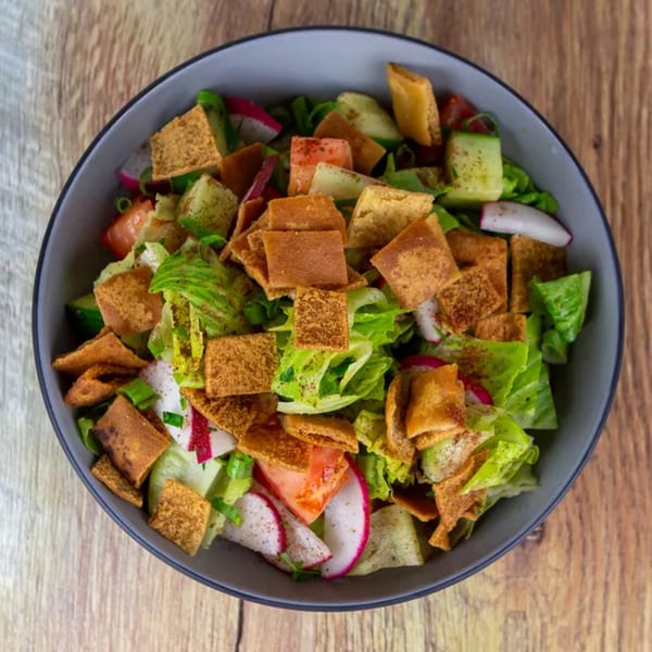 A vibrant fattoush salad in a dark bowl, featuring crisp lettuce, radishes, tomatoes, and toasted pita.