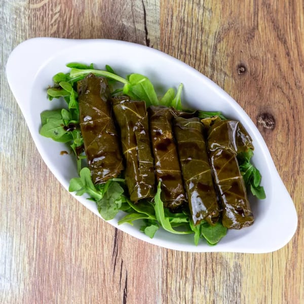 Five dolmades, or stuffed grape leaves, on a bed of fresh arugula in a white dish.
