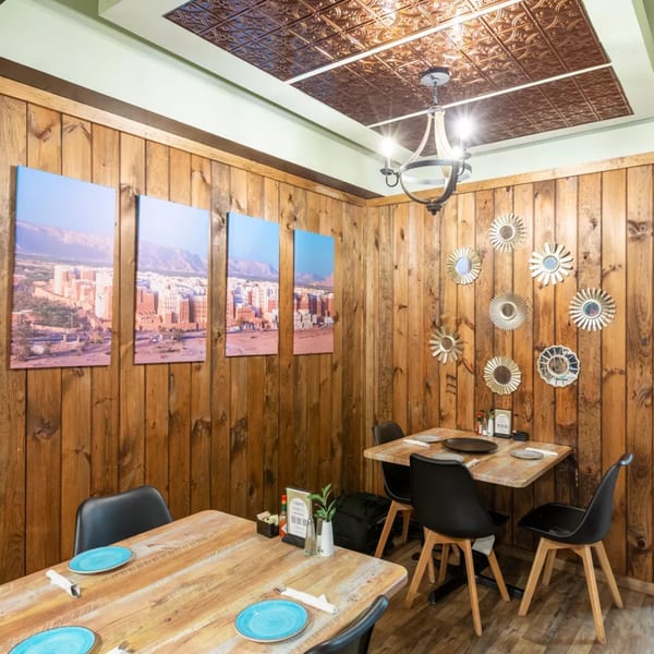 Restaurant interior with wooden walls, tables set with blue plates, and city landscape artwork.