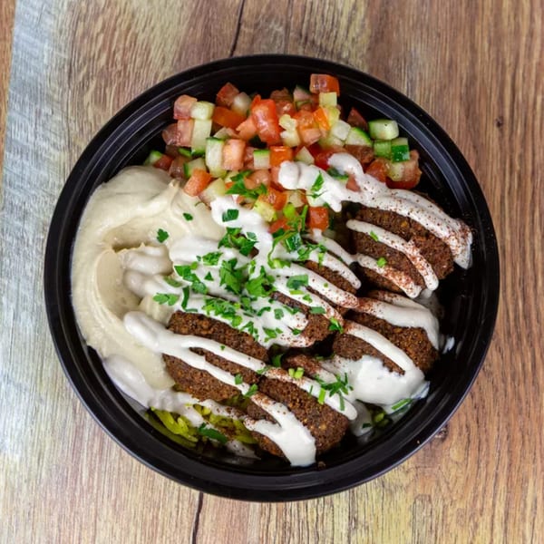 Falafel bowl with hummus, diced tomatoes, cucumbers, and white sauce, garnished with parsley.