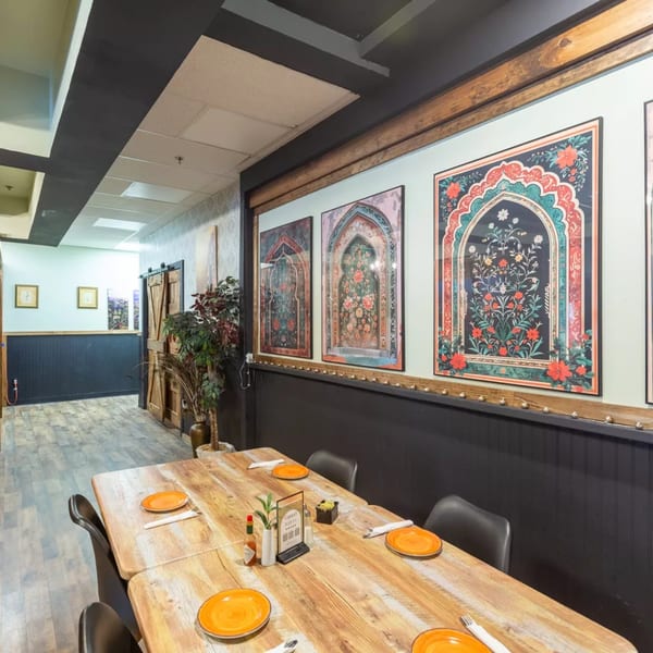 A restaurant dining area with a long wooden table set with orange plates and decorative wall art.