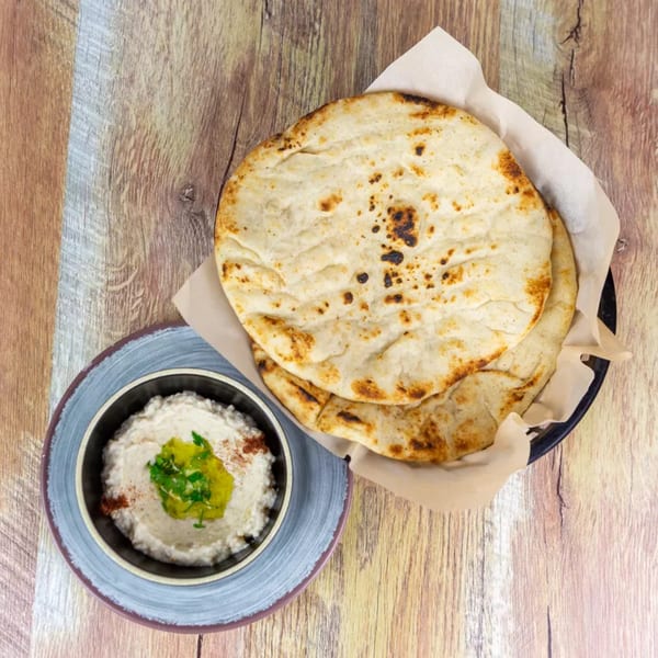 Flatbread in a basket next to a bowl of hummus with olive oil and parsley.