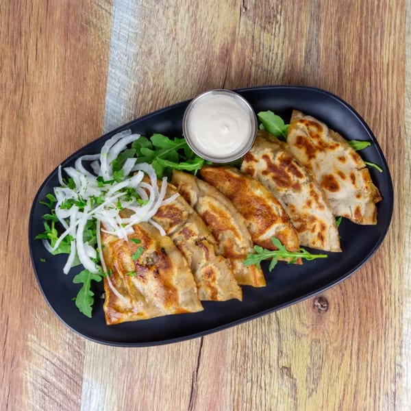 A black oval plate of golden-brown fried dumplings with arugula, sliced onions, and a white dipping sauce.