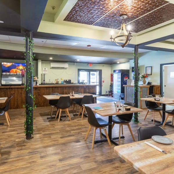 A restaurant dining area with wooden tables, black chairs, a bar, and a patterned ceiling.