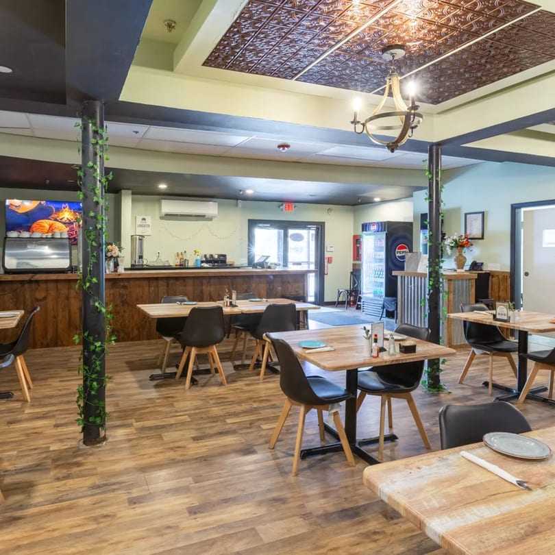 A restaurant dining area with wooden tables, black chairs, a bar, and a patterned ceiling.